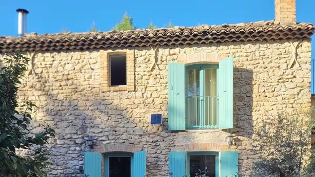 Un bâtiment en pierre avec des volets bleus, une cheminée et une petite fenêtre.