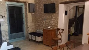 Un coin repas avec une table et des chaises en bois, une petite table ronde, un téléviseur fixé au mur et un mur en pierre.