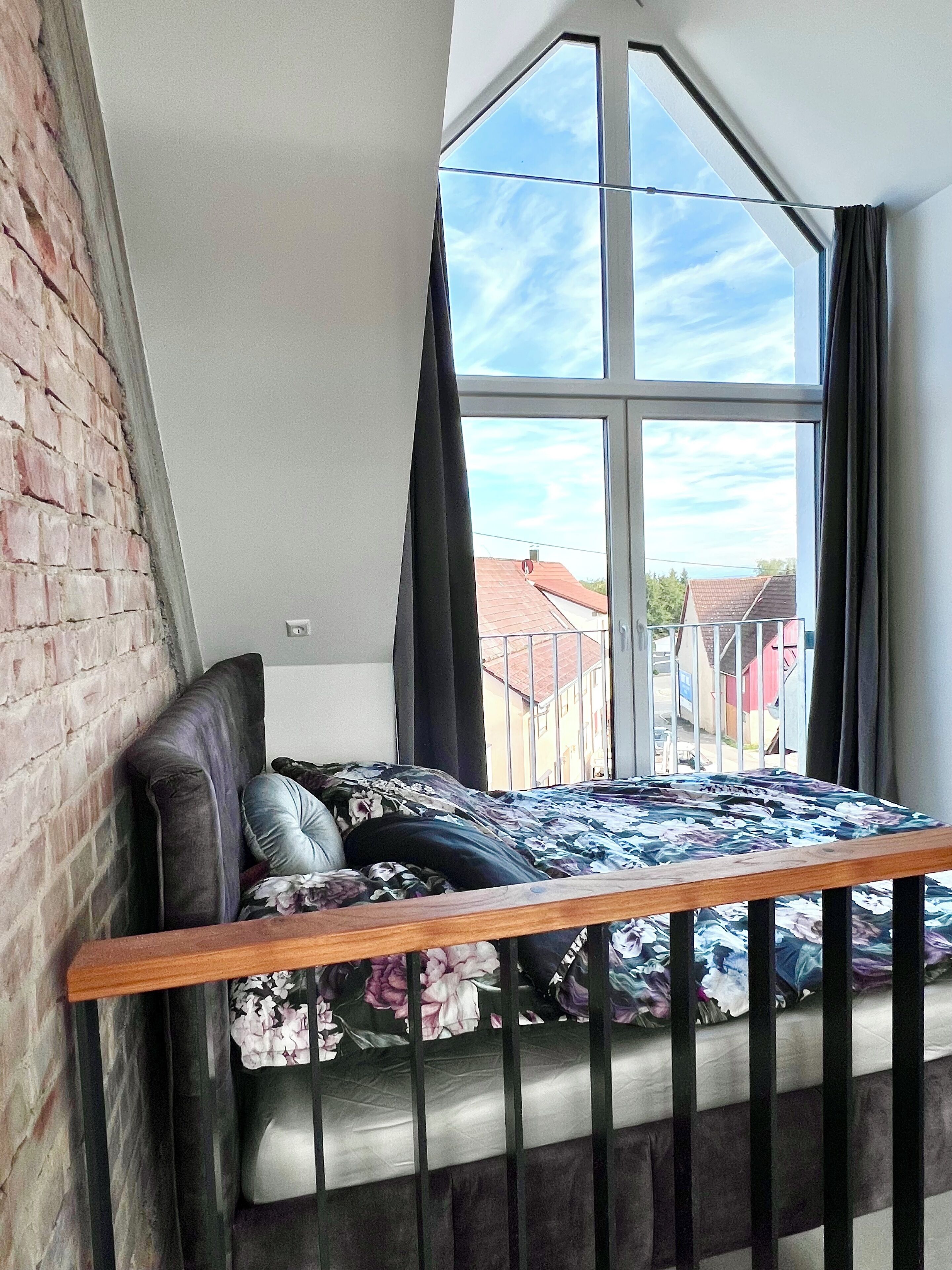 A loft bedroom with a sloped ceiling, a large window, and a view of the neighborhood.
