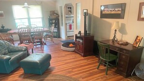 Sala de estar com sofá, puf, tapete, mesa de jantar com cadeiras e um rack para televisão.