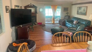 Uma sala de estar com televisão de tela plana, lareira, sofá e uma área de jantar com cadeiras.
