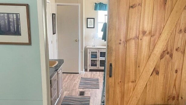 Um corredor com uma porta de madeira estilo celeiro, uma área de cozinha com pia e armários, e um quadro na parede.