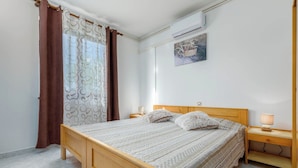 Quarto com cama de madeira, mesa de cabeceira com luminária, ar condicionado fixado na parede e um quadro emoldurado.