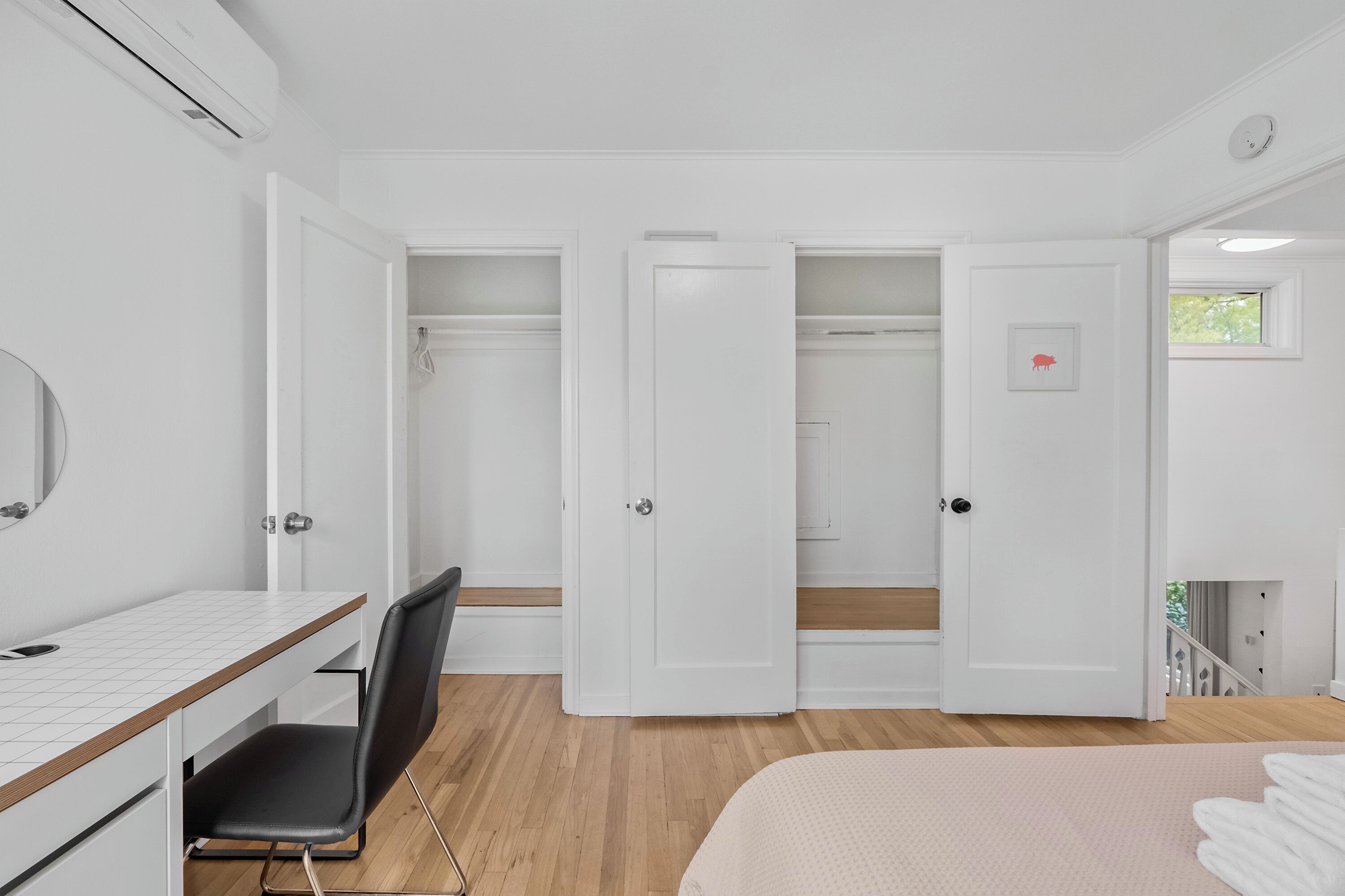 A bedroom with a bed, a desk, and a chair. There are two doors, one of which is open.