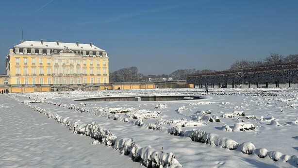 Un edificio grande e histórico con varios pisos y una fachada simétrica, rodeado de nieve y árboles.