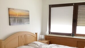 Un dormitorio con cama de madera, una mesita de noche, una lámpara y un cuadro en la pared, además de una ventana con persianas.