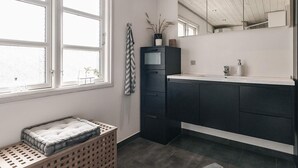 Un baño moderno con un ventanal grande, muebles oscuros, un espejo y una planta pequeña.