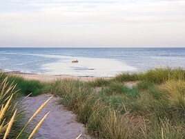 Una playa con un bote en el agua, dunas cubiertas de hierba y cielo despejado.