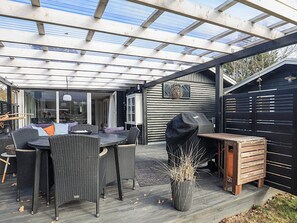 Une terrasse extérieure dotée d’un espace salon couvert, d’un barbecue et d’une plateforme en bois.