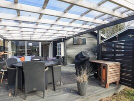 Un patio exterior con una zona de estar cubierta, una parrilla y una terraza de madera.