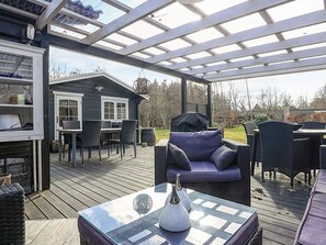 Une terrasse extérieure couverte comprenant un espace repas, un barbecue et une petite maison avec une fenêtre.