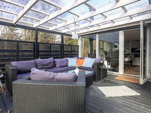 Une terrasse extérieure avec un canapé, une table et une porte vitrée donnant sur un espace intérieur.