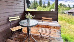 A wooden deck with a round table and two chairs, a vase with flowers, and a view of trees and sky. - 4 Person Holiday Home in Gol (Gol)