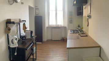 A kitchen with a stove, sink, and a window. There is a radiator under the window and a small stool.