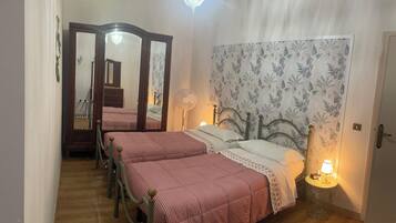A bedroom with two beds, a mirror, a chandelier, and floral wallpaper.