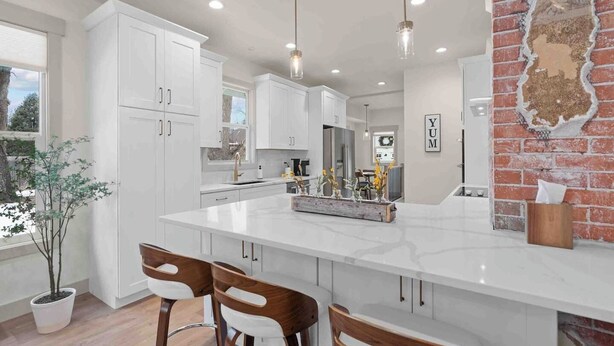 Una cocina moderna con armarios blancos, una isla grande, iluminación colgante y una pared de ladrillo decorativa.