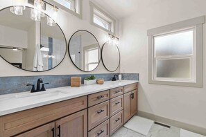 A bathroom with three large mirrors, a white sink, wooden cabinets, and a window.