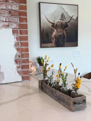 A rustic wooden planter with yellow flowers on a polished floor, a brick wall, and a framed picture of a bull on the wall.