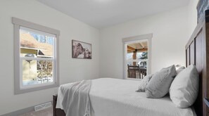 A bedroom with a bed, two windows, a ceiling fan, and a wall-mounted picture.
