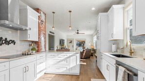 Una cocina moderna con armarios blancos, una pared de ladrillo decorativa, iluminación colgante y una isla central.