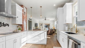Una cocina moderna con armarios blancos, una pared de ladrillo decorativa, iluminación colgante y una isla central.