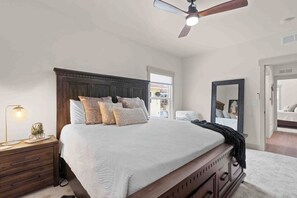 A bedroom with a large bed, a ceiling fan, a nightstand, a lamp, and a mirror.