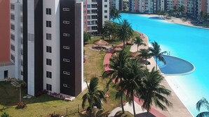 Een modern appartementencomplex met een zwembad, palmbomen en een rode pad.