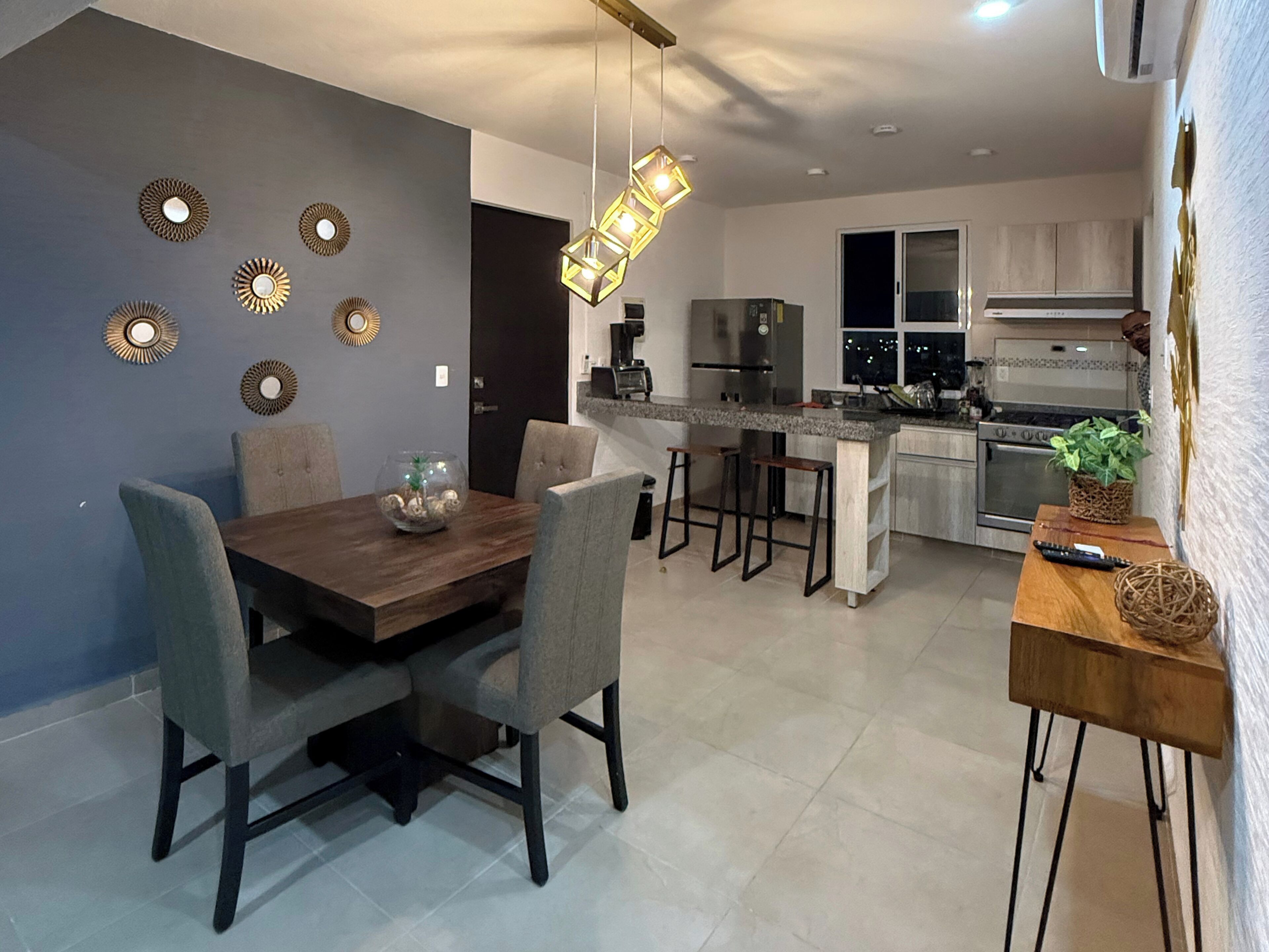 Una cocina moderna con una isla central, electrodomésticos integrados y un comedor con mesa y sillas de madera.