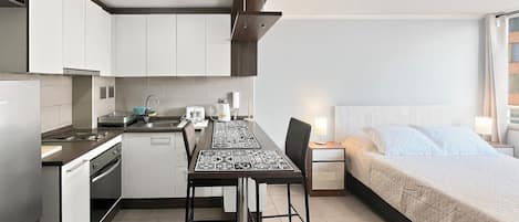 A compact hotel room with a kitchenette, a dining area, and a bed.