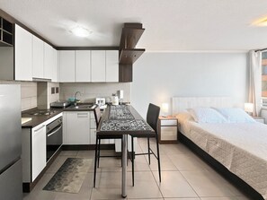 Een compact hotelkamer met een kitchenette, een eethoek en een bed.