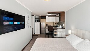 A modern hotel room with a bed, a desk, and a kitchenette.
