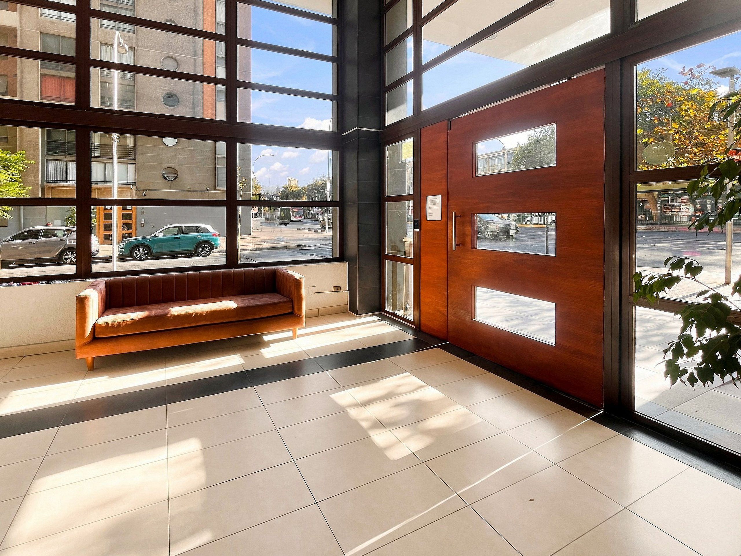 A lobby with a wooden bench, large windows, and a view of the street.