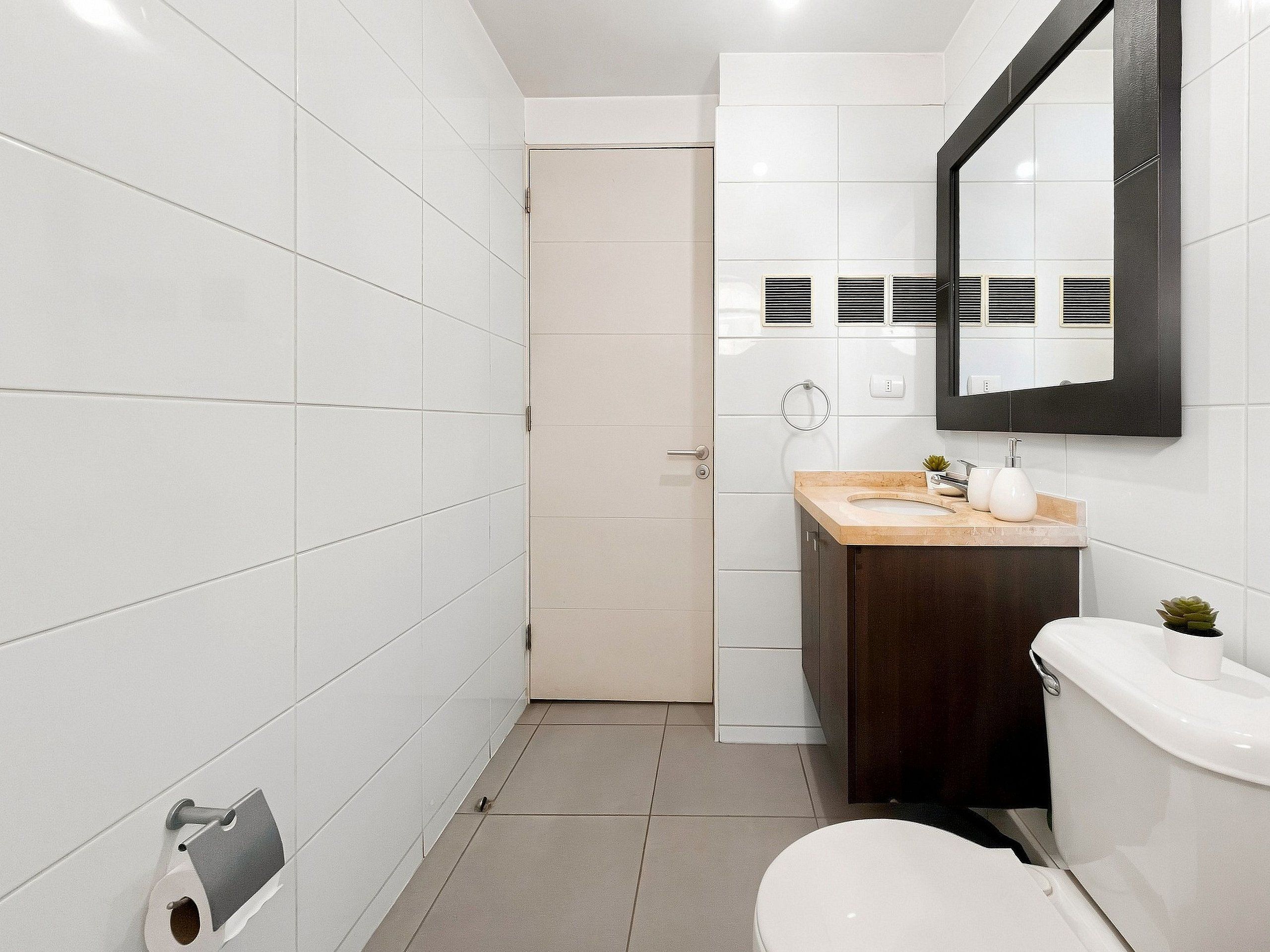A modern bathroom with white tiles, a toilet, a sink with a mirror, and a shower area.