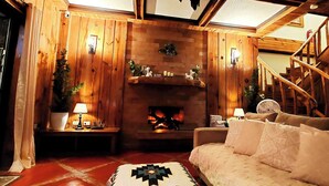 Una sala de estar acogedora con chimenea, paredes de madera, un sofá y una escalera.