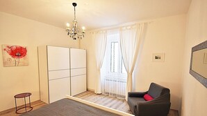 A bedroom with a bed, a chair, a wardrobe, a chandelier, and a window with curtains. - Apartment in Valbandon Near Adriatic Beach (Fazana)