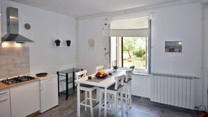 A modern kitchen with a gas stove, white cabinets, a dining table with chairs, and a window with a view of greenery. - Apartment in Valbandon Near Adriatic Beach (Fazana)