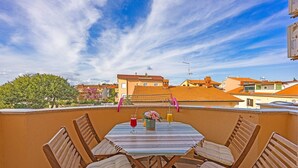 Eine Dachterrasse mit einem Tisch für zwei Personen, einem Stuhl und Blick auf die Stadtlandschaft.