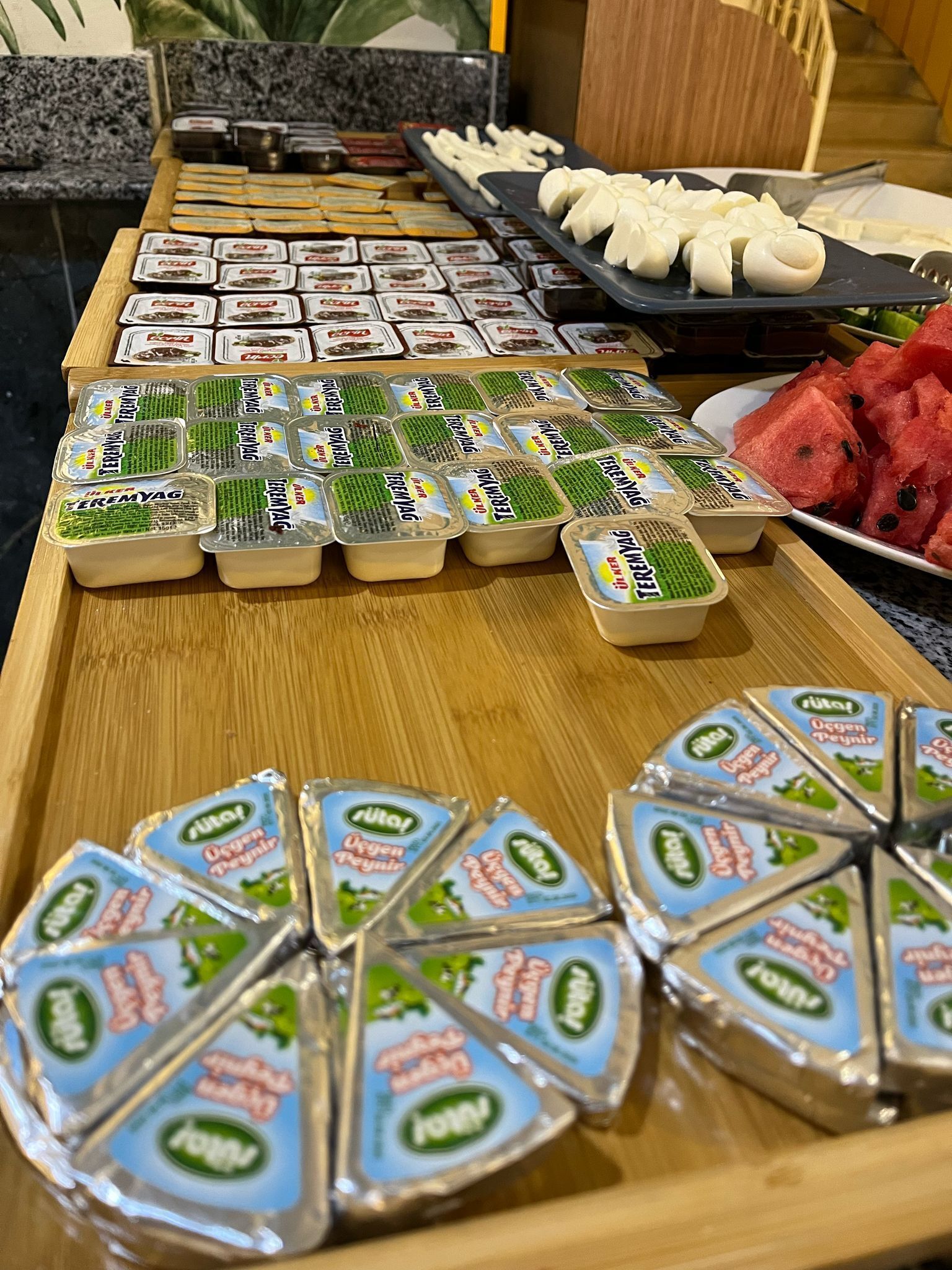 Een buffet met verschillende soorten eten, zoals verpakte yoghurt, brood en watermeloen.