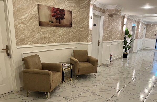 A hallway with marble walls, two beige armchairs, a small table, and a painting. - HOTEL GAZİ (Gaziantep)