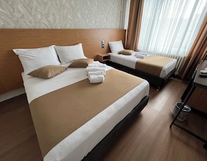 A hotel room with two beds, each with white linens and brown throw pillows. There is a wooden headboard, a small wooden nightstand, and a window with curtains. - HOTEL GAZİ (Gaziantep)