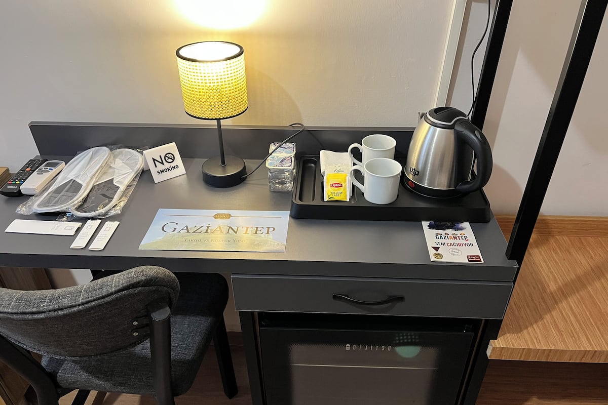Ein Hotel-Schreibtisch mit Lampe, Tablett mit Tassen, Wasserkocher, Schild und Minibar.