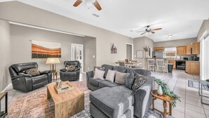 A spacious living area with a grey sofa set, a wooden coffee table, and a dining table with chairs. A kitchen with wooden cabinets and a black dishwasher is visible in the background. - Pet Friendly Home near Downtown Weatherford! Bring the Family, Relax & Enjoy! (Weatherford)