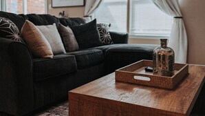 A living room with a dark-colored sofa, a wooden coffee table with a decorative bottle, and a patterned rug. - Pet Friendly Home near Downtown Weatherford! Bring the Family, Relax & Enjoy! (Weatherford)
