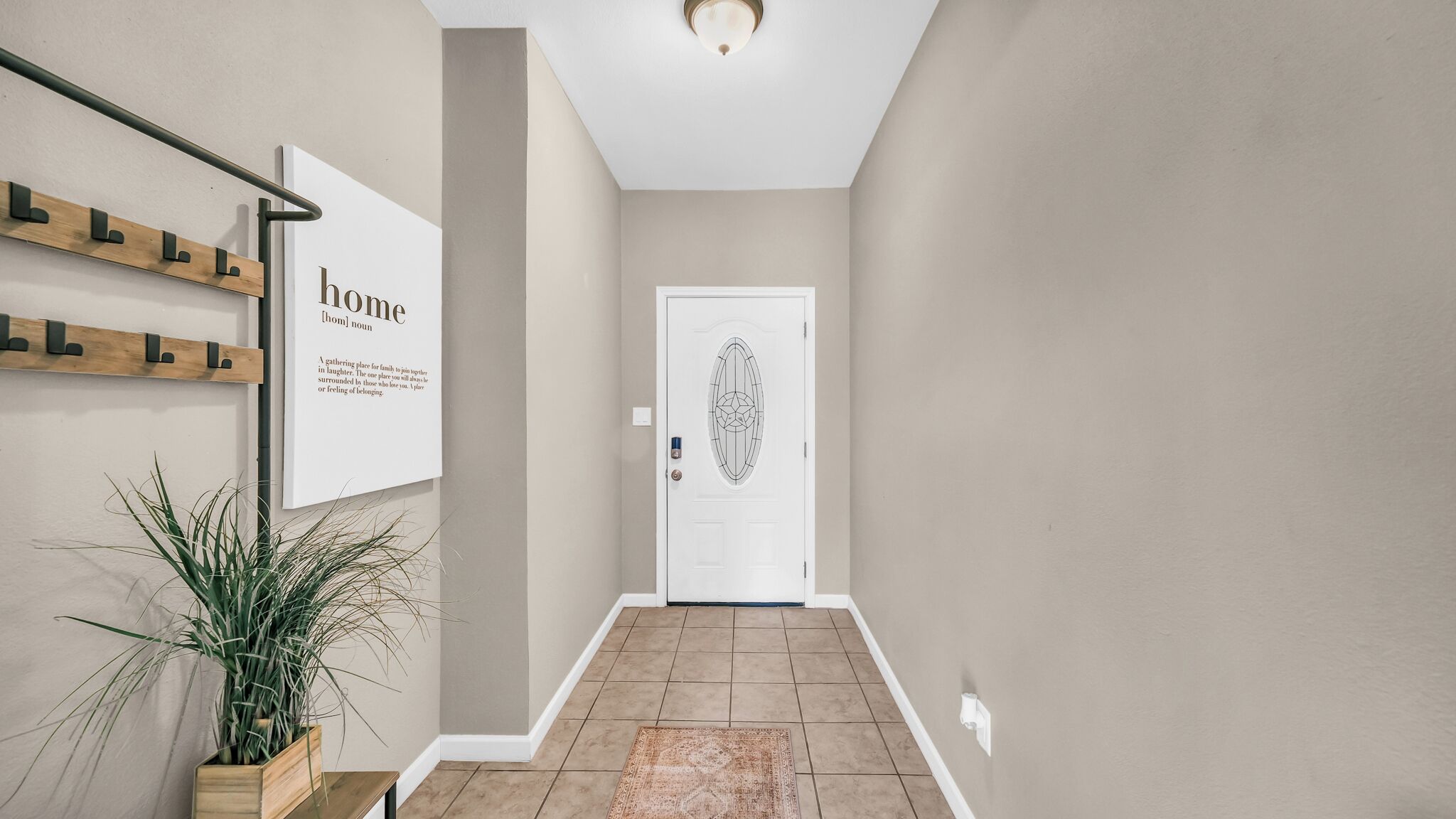 A hallway with a white door, a wall-mounted sign, a plant, and a tiled floor.