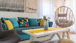 A living room with a teal sofa, a white coffee table, a hanging chair, and two wall-mounted paintings. - Apartment With Shared Swimming Pool (Liznjan)