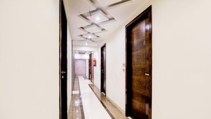 Un pasillo de hotel con suelo de baldosas, una puerta de madera a la derecha e iluminación empotrada en el techo.