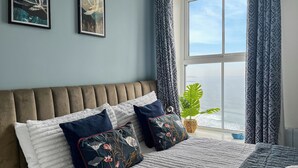 Ein Schlafzimmer mit einem großen Bett, Meerblick und zwei gerahmten Kunstwerken an der Wand.