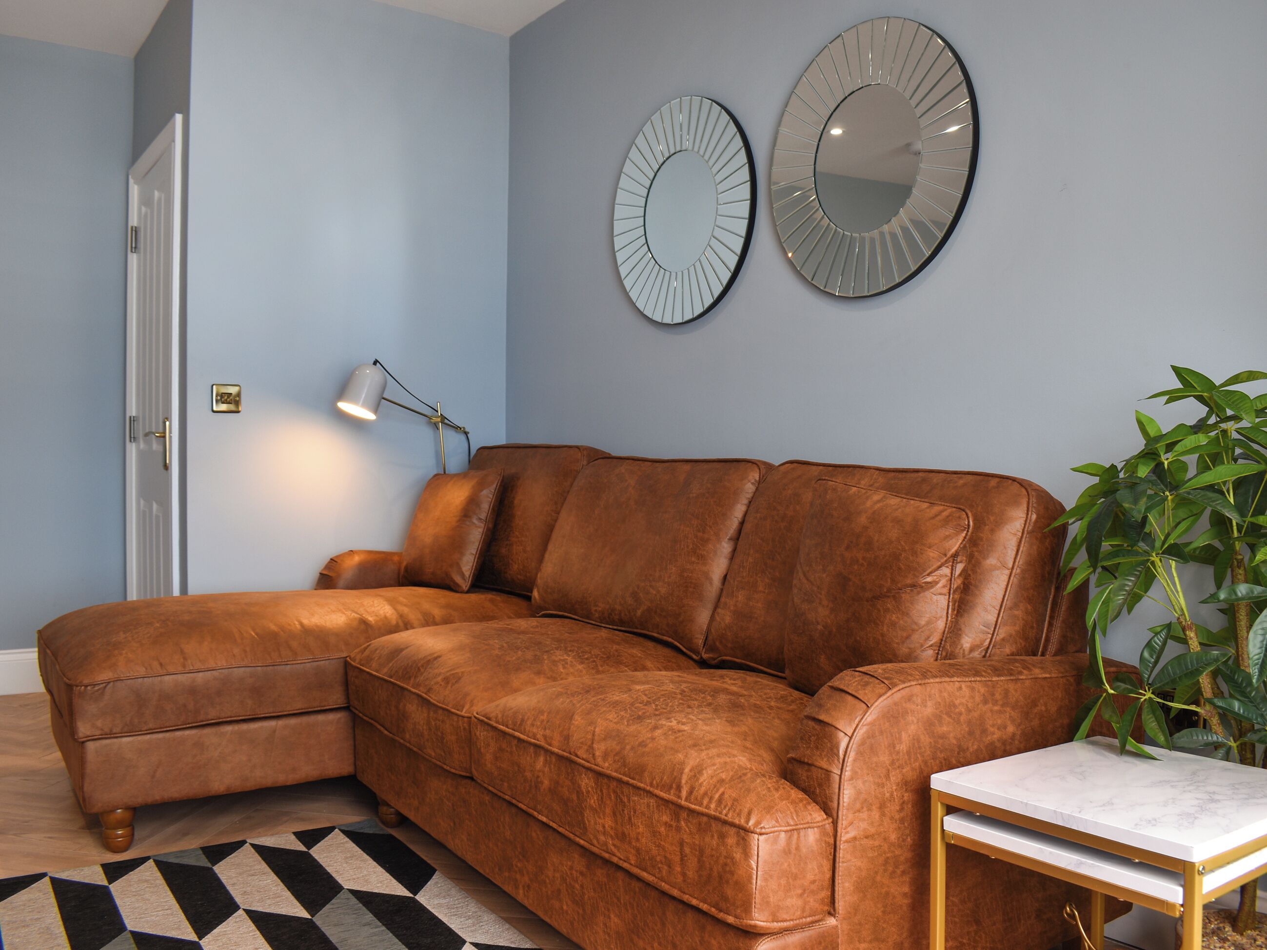 A brown leather sectional sofa, a small table with a white marble top, and two wall mirrors.
