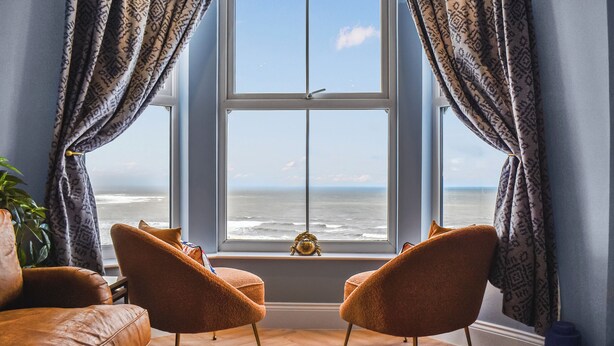 Ein Zimmer mit großem Fenster und Meerblick, zwei Sessel und eine Pflanze.