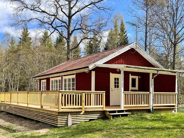 Een rode houten hut met een veranda, omringd door bomen.